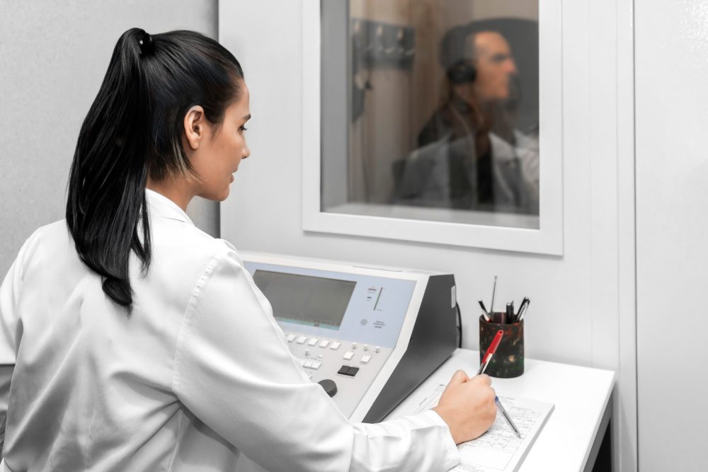 Audiologist woman doing the hearing exam to a mixed race man patient using an audiometer in a special audio room.